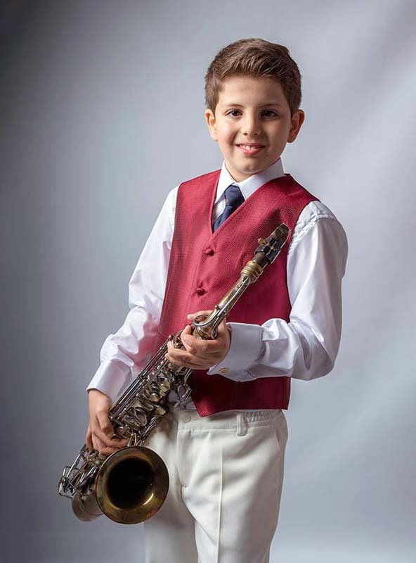 Fotografía de comunión con aficiones. Niño con saxofón en un ambiente minimalista de estudio