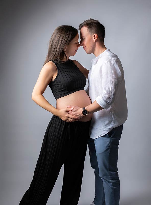 Pareja de futuros padres embarazados con gesto cómplice y feliz. Sesión de fotografía de embarazo emotiva.