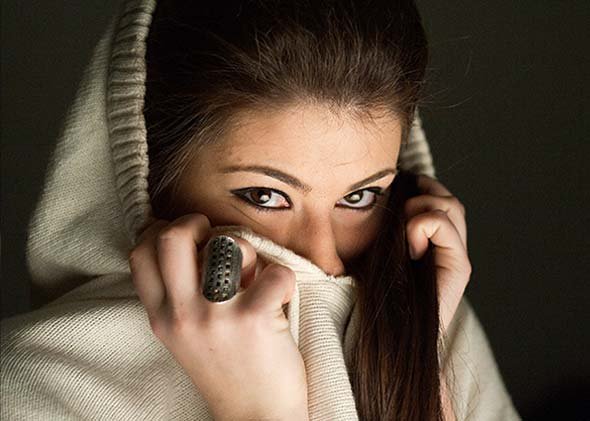 Retrato en primer plano de chica con expresión enigmática, cubriéndose la boca mientras mira a cámara.